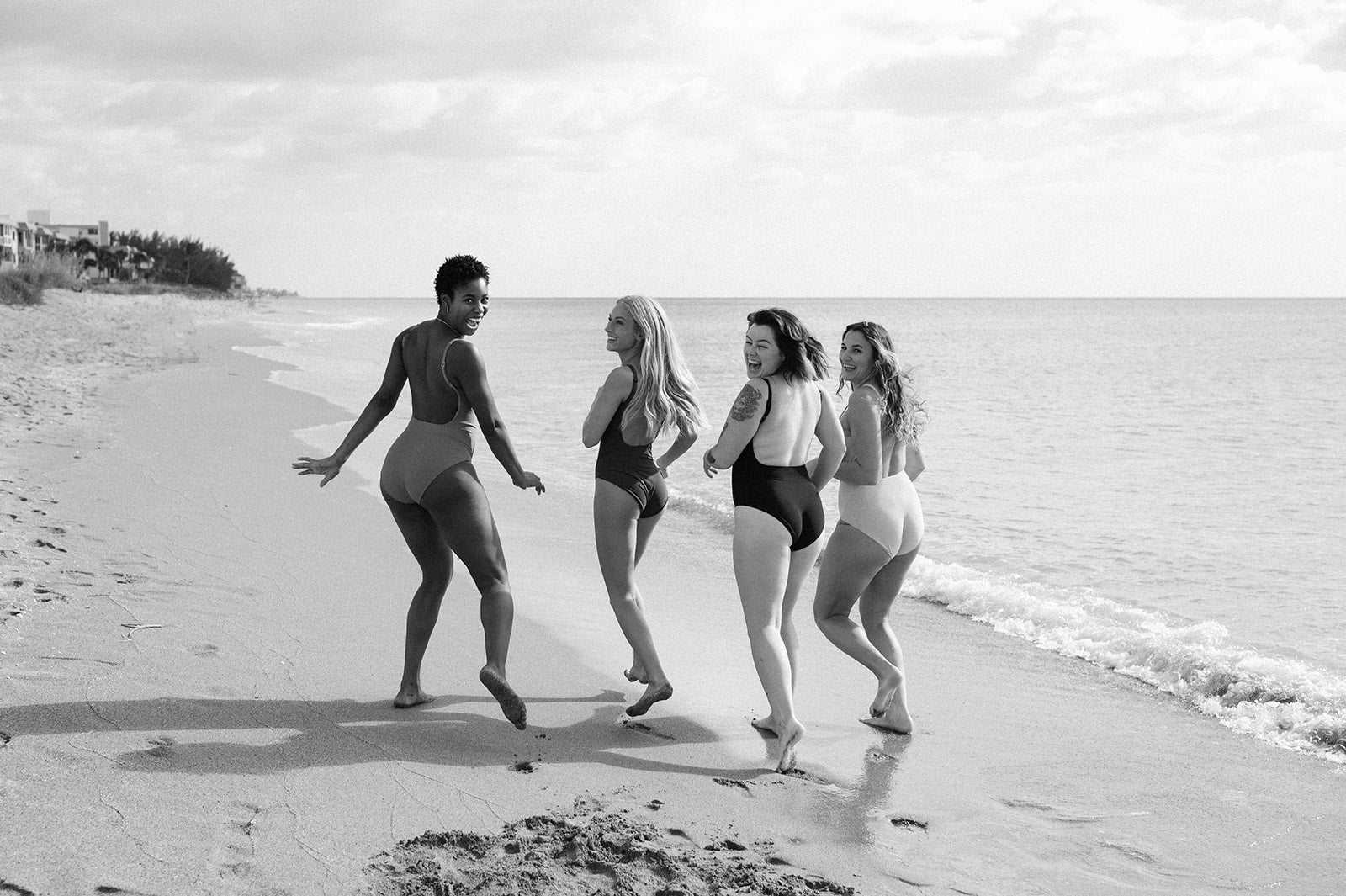 four models laughing and running away on the beach looking back at camera